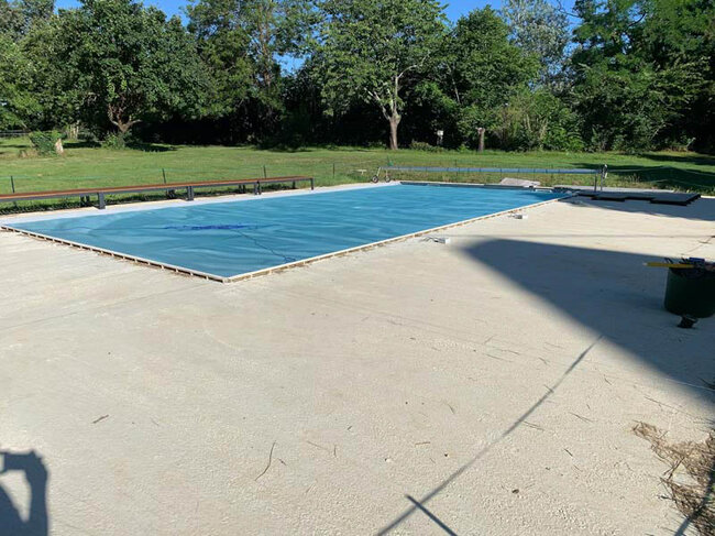 Piscina doméstica con persiana protectora azul en un entorno grande