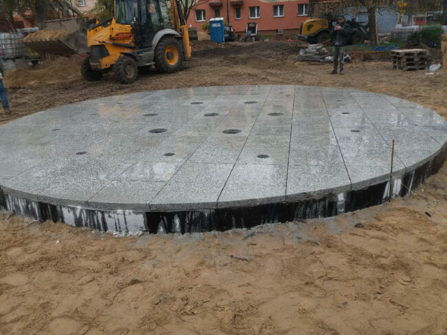 Construcción de una fuente circular urbana con baldosas de granito gris en la plaza