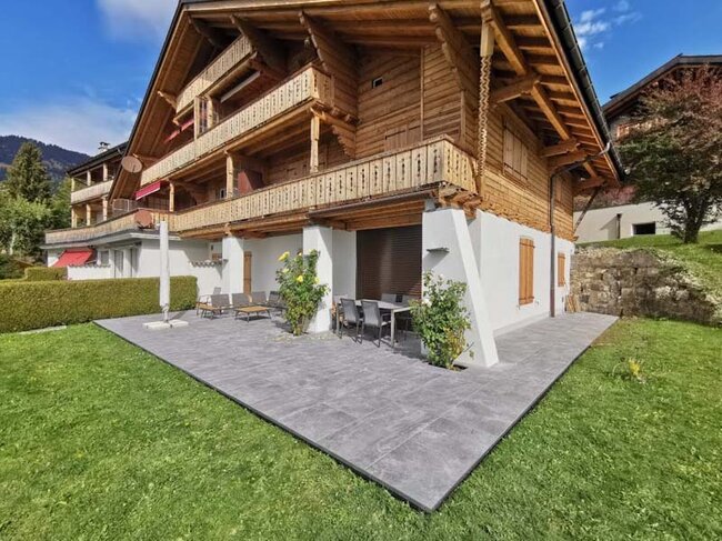 Terraza con suelo técnico con baldosas de gres oscuras junto a una casa de madera de estilo alpino