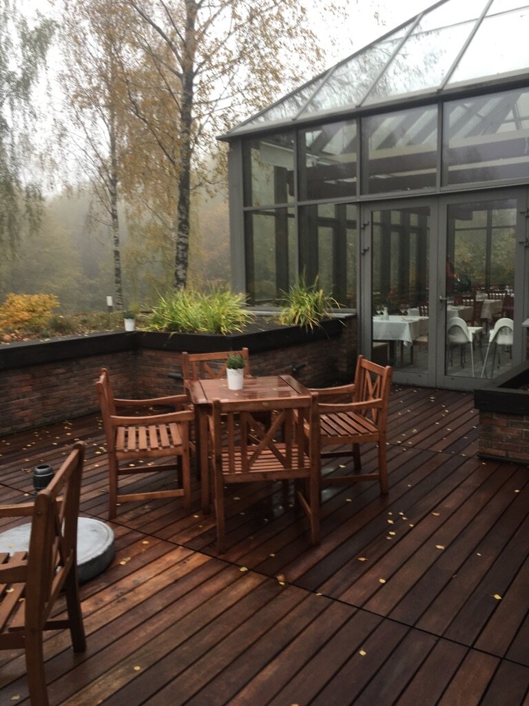 Terraza de madera con muebles y jardín de invierno al fondo
