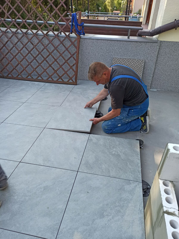 Profesional colocando baldosas de gres grises sobre soportes de terraza