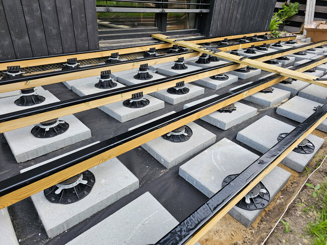 Subestructura de terraza con vigas de madera sobre plots soporte y baldosas de hormigón