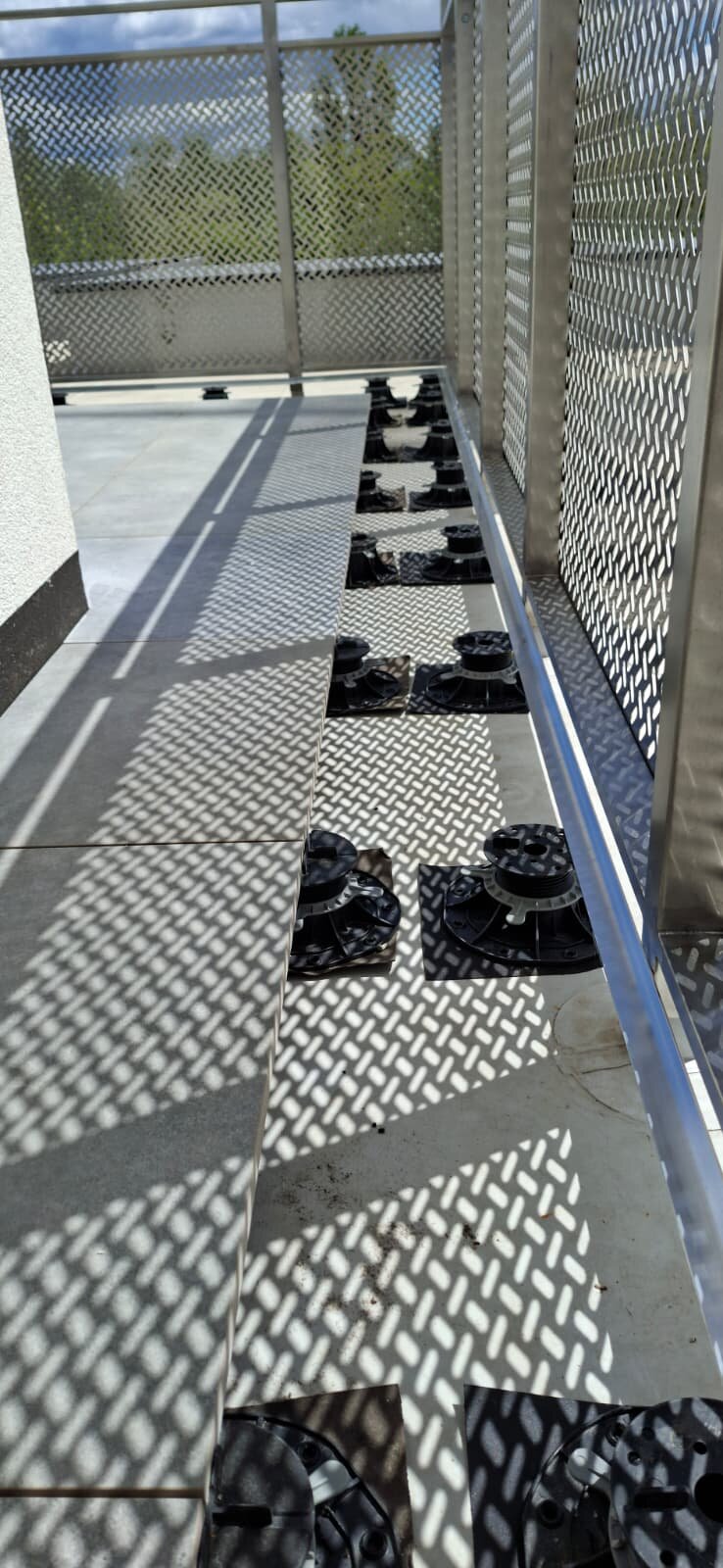 Soportes regulables bajo baldosas de terraza junto a la barandilla