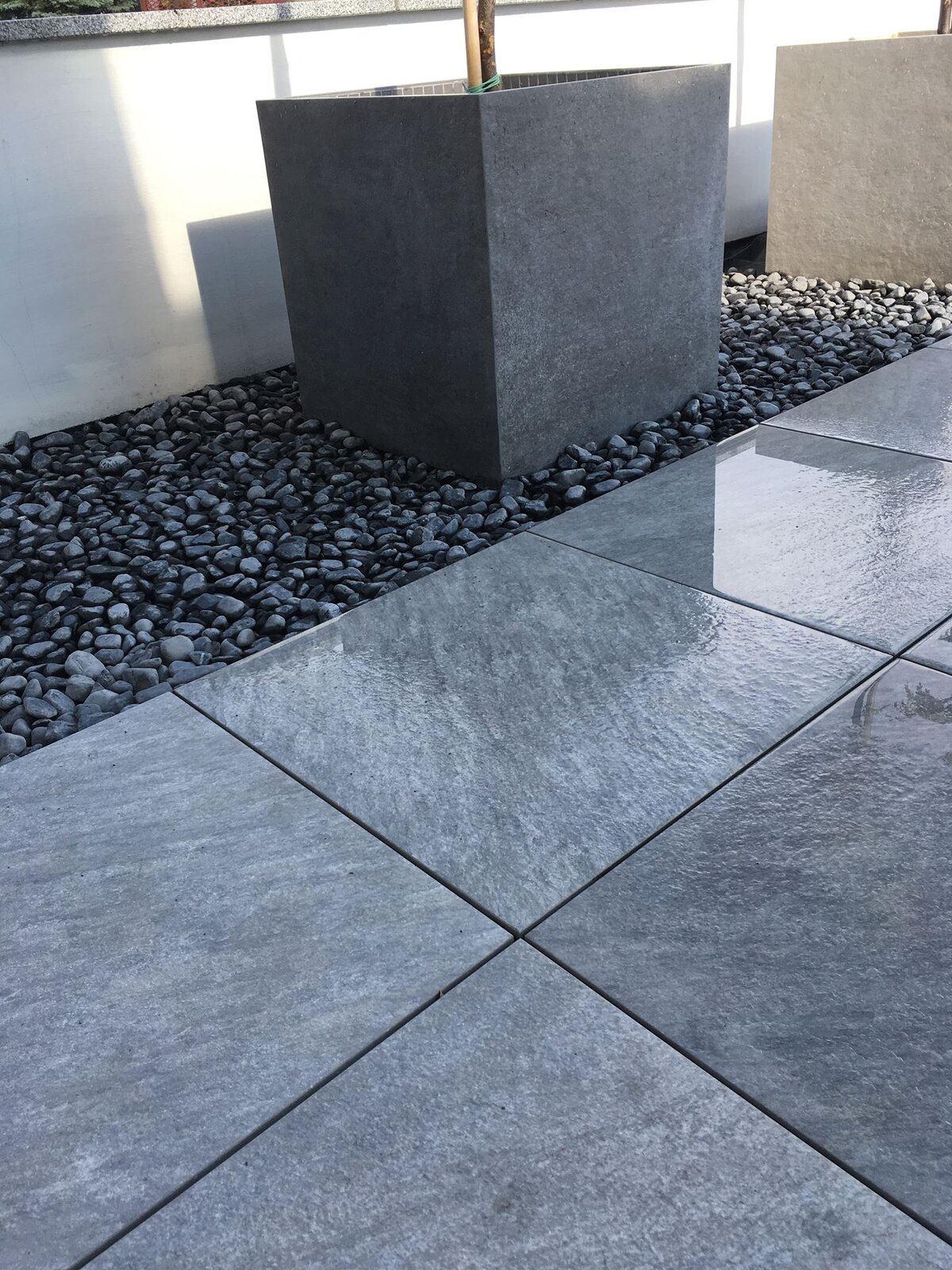 Grey porcelain tiles on the terrace with a stone border and planter