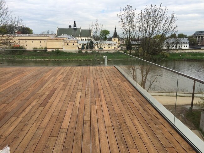Larga terraza de madera en el balcón con barandilla de vidrio