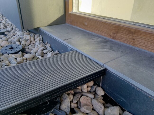 Montaje de tabla de terraza junto a puertas balconeras sobre plots soporte y grava