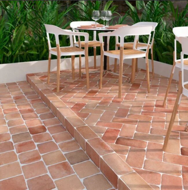 Terraza con baldosas de terracota con muebles de jardín y vegetación al fondo