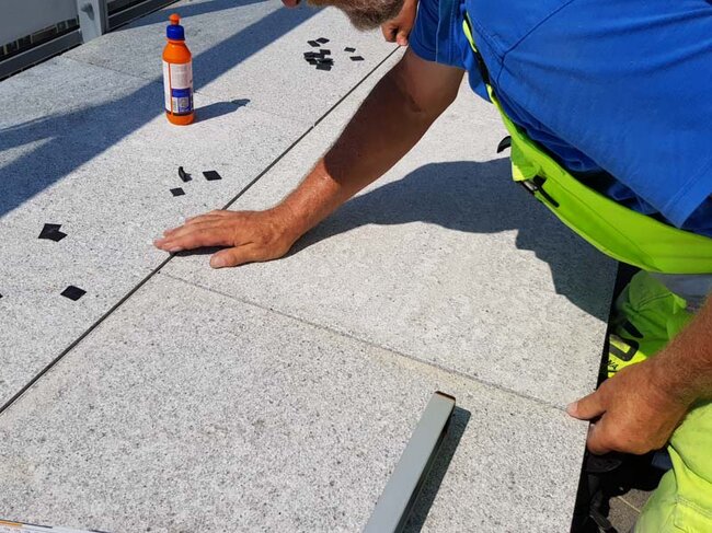 Hombre colocando baldosas de terraza sobre plots soporte regulables en una terraza