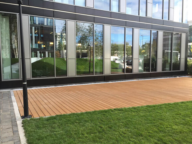 Terraza sobre el terreno junto a un edificio de oficinas acabada con tablas de composite