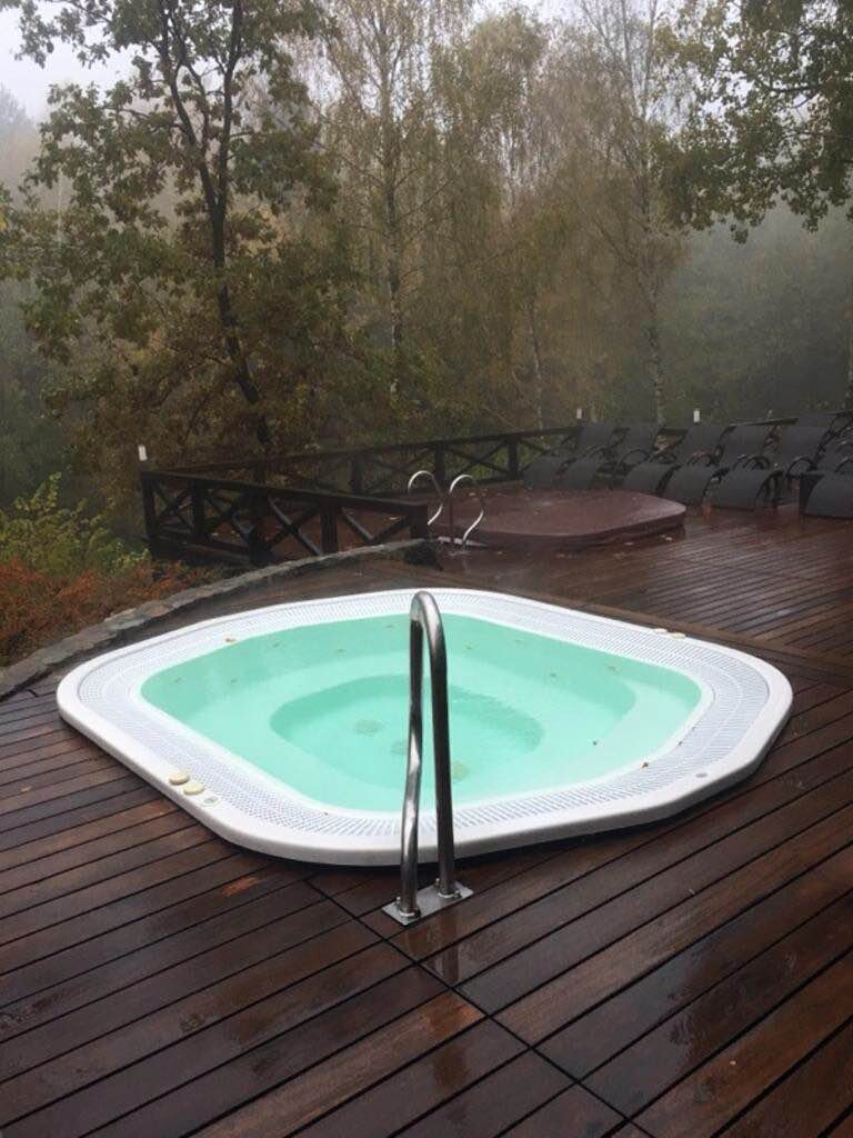 Jacuzzi de jardín empotrado en una terraza de madera rodeada de bosque.