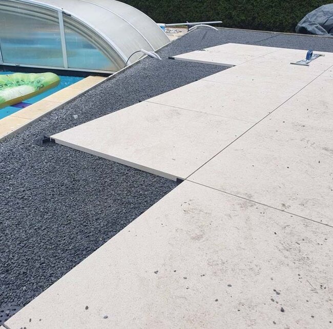 Colocación de baldosas claras de terraza sobre soportes sobre una base de grava junto a la piscina.