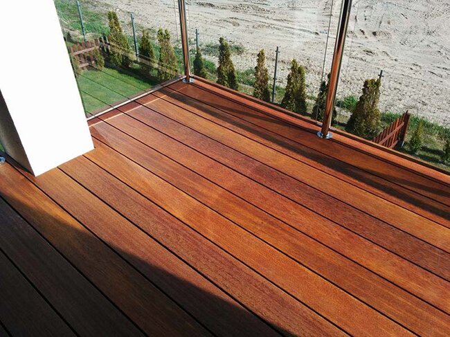 Balcón acabado con tablas de madera exótica con barandilla de vidrio.