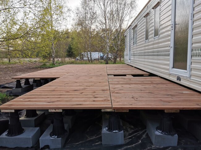 Construcción de terraza con tablas de madera sobre plots soporte regulables altos.