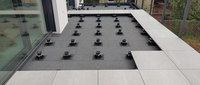 Montaje de terraza con suelo técnico con baldosas de gres gris claro sobre plots soporte regulables negros.