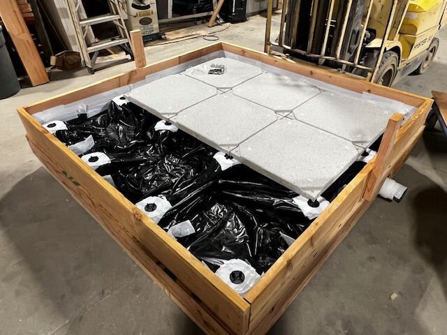 Gran marco de soporte de madera con revestimiento de plástico negro y baldosas de porcelana de color gris claro instaladas en una azotea