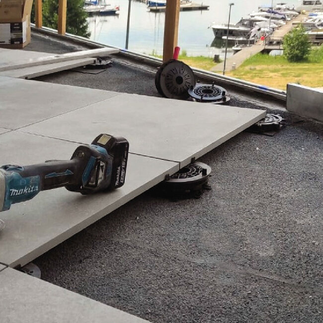 Instalación de baldosas de terraza de porcelana para exteriores sobre plots soporte regulables de plástico de bajo perfil con una herramienta eléctrica inalámbrica.