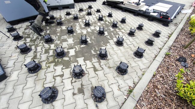 Disposición de cuadrícula de soportes regulables de plástico colocados sobre adoquines para la instalación de una terraza exterior