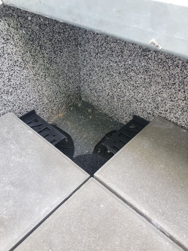 Colocación en esquina de plots soporte de terraza recortados que sostienen baldosas elevadas exteriores junto a una pared texturizada.
