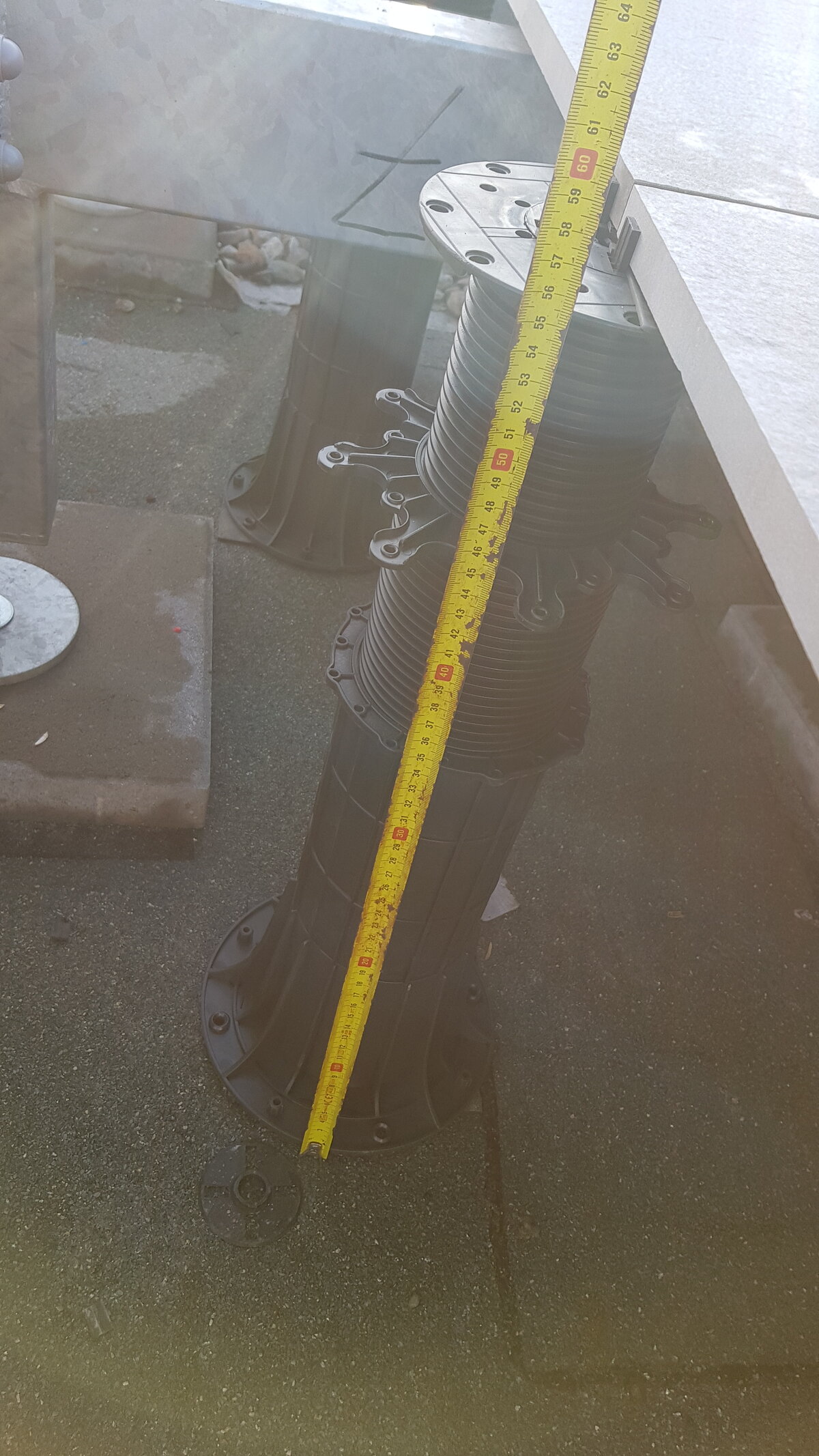Yellow tape measure checking the elevation height of an extended plastic paving pedestal riser.