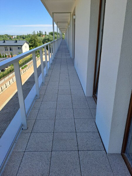 Pavimento de terraza exterior largo terminado con baldosas de terraza de textura de hormigón y barandillas blancas.
