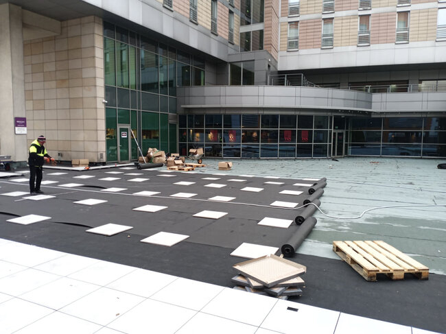 Trabajador de la construcción instalando plots soporte de terraza y membrana base en la azotea de un edificio comercial.