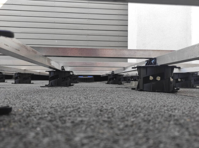 Vista desde un ángulo bajo de vigas de terraza de aluminio apoyadas por plots soporte regulables de bajo perfil en una terraza.