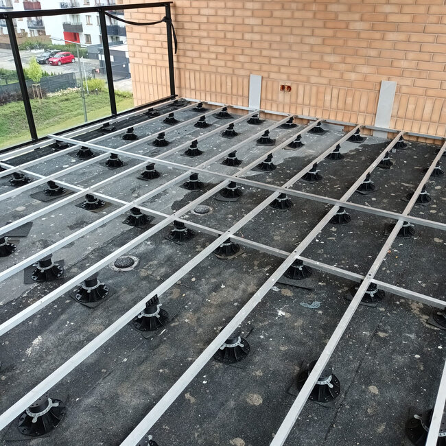 Subestructura de rejilla de vigas de aluminio apoyada sobre plots soporte regulables en una terraza de techo.