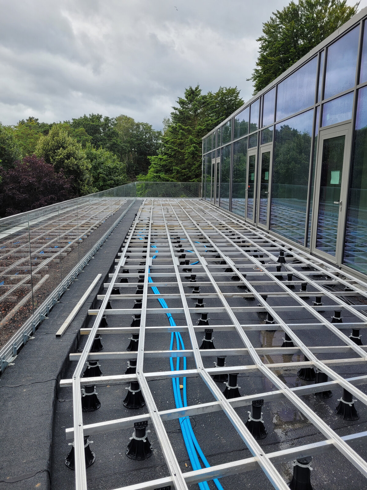 Estructura de vigas de aluminio montada sobre soportes de terraza de plástico regulables para suelos de terraza en exteriores.