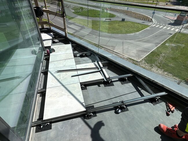 Vista superior de una instalación de suelo elevado de balcón con baldosas de porcelana sobre vigas de aluminio y plots soporte regulables de plástico.