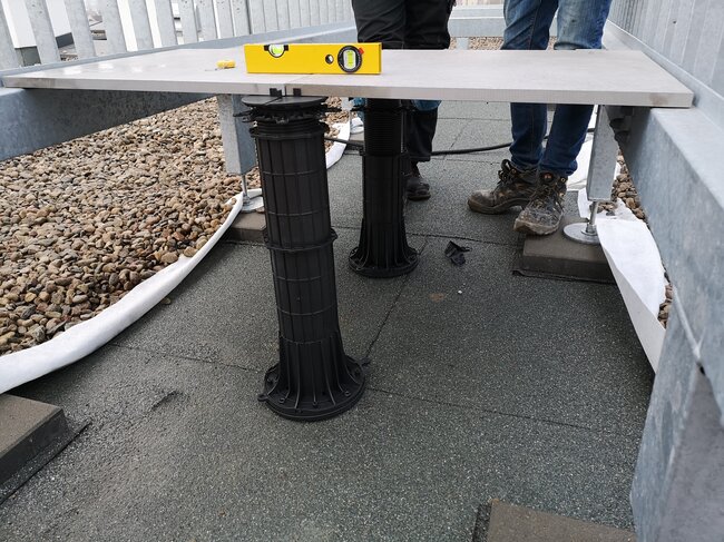 Leveling outdoor patio tiles using tall adjustable plastic pedestals and spirit level.
