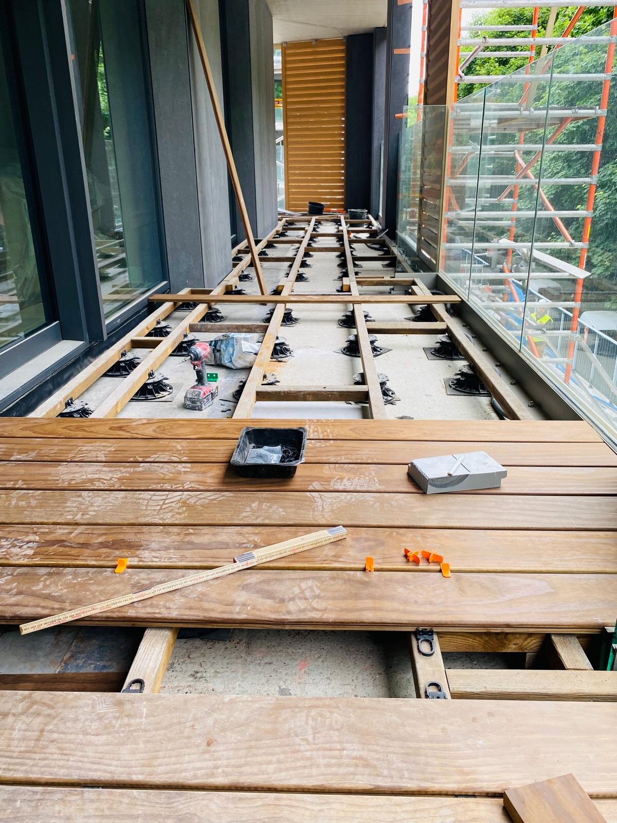 Instalación de terraza de balcón con tablas de terraza de madera dura colocadas sobre una subestructura de plots soporte regulables.