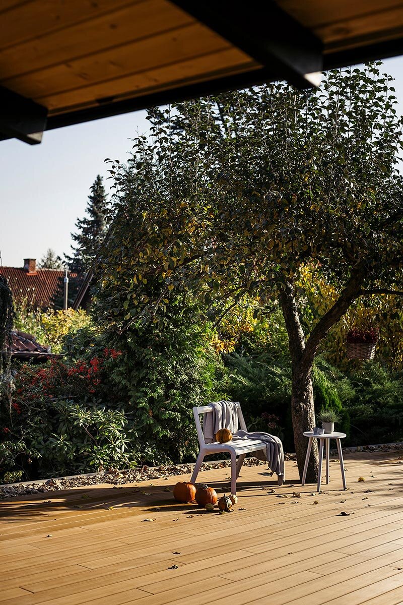 Acogedora terraza de jardín con modernas baldosas de composite decorada con calabazas de otoño y muebles de jardín.