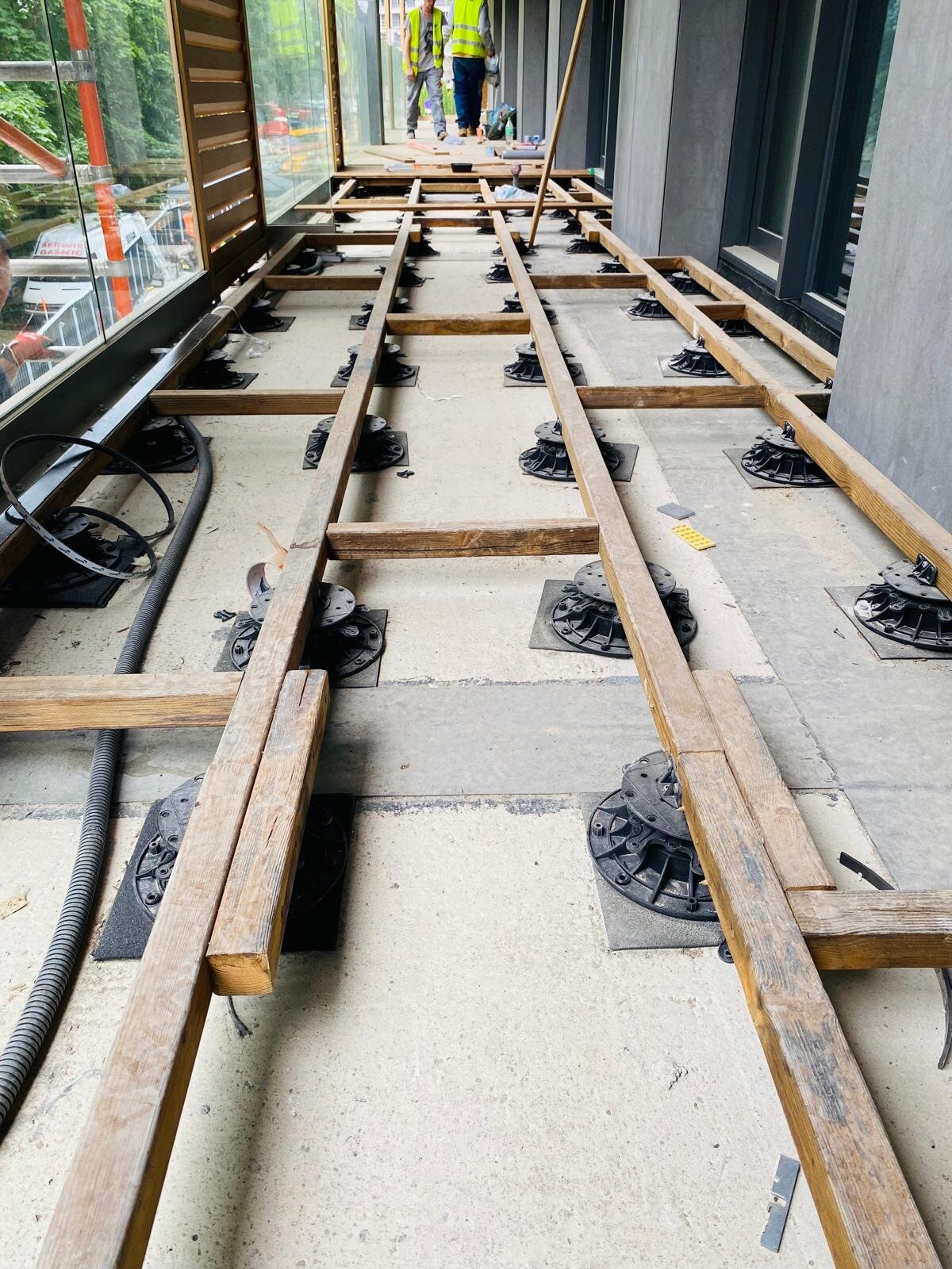Plots soporte de terraza regulables y subestructura de vigas de madera montados en una terraza de balcón.