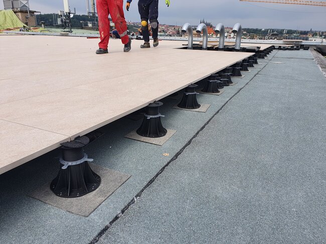 Trabajadores caminando sobre un sistema de pavimento elevado con plots soporte parcialmente instalado en una azotea.