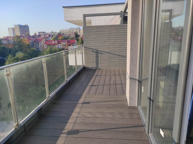 Balcón de apartamento moderno con tarimas de composite, barandillas de vidrio y mampara de privacidad.