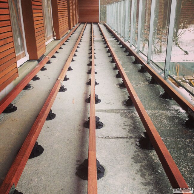 Estructura larga de subestructura de terraza de balcón con vigas de madera paralelas montadas sobre soportes regulables.