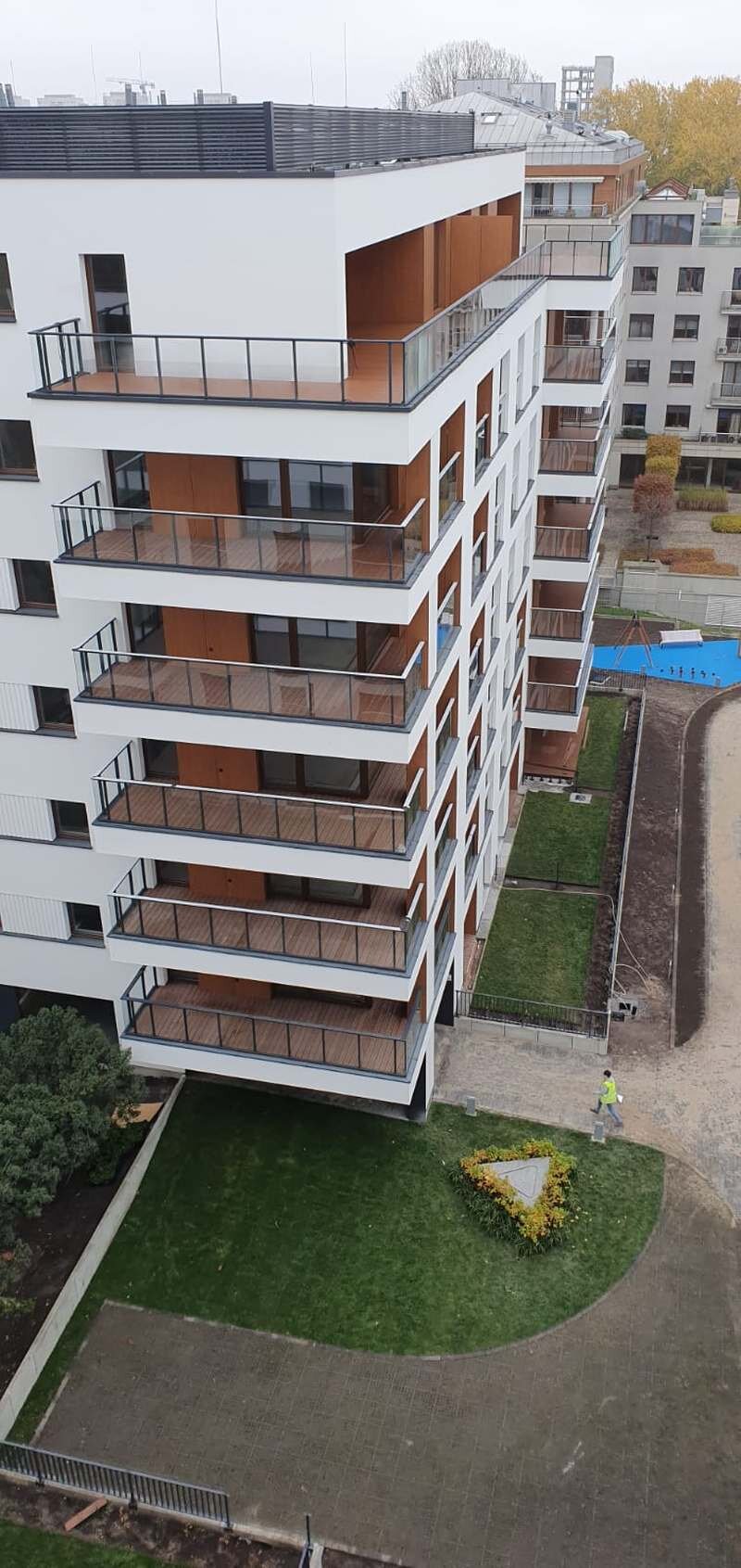 Vista exterior de un moderno edificio residencial de varias plantas con balcones acabados en madera y barandillas de cristal.