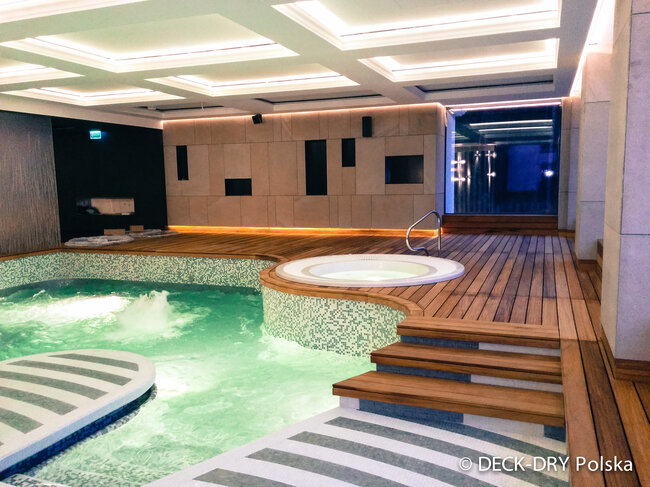 Terraza de madera elevada instalada sobre una piscina cubierta utilizando plots soporte regulables.