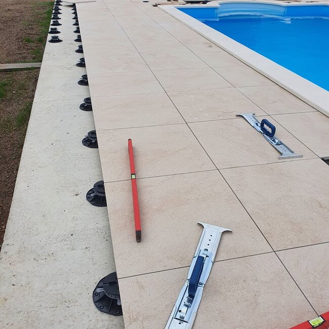 Instalación de baldosas de gres porcelánico sobre plots soporte regulables alrededor de la piscina.