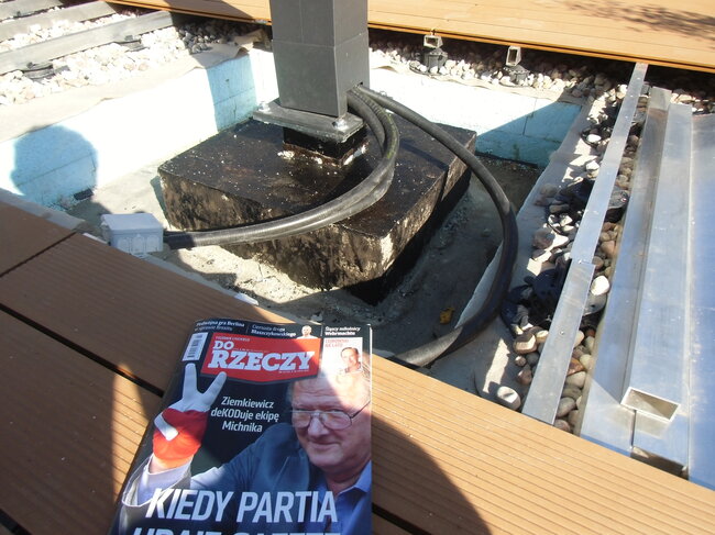 Cable eléctrico tendido a lo largo de la base del poste y de la estructura de grava subyacente bajo una terraza elevada con suelo técnico.