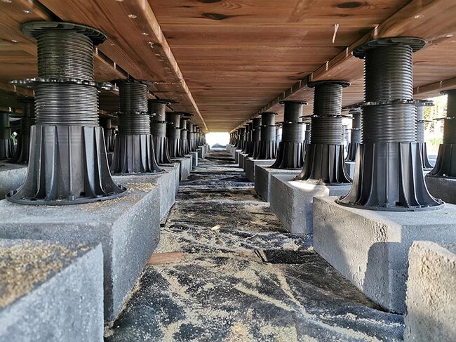 Adjustable pedestals mounted on concrete blocks under a wooden terrace deck.