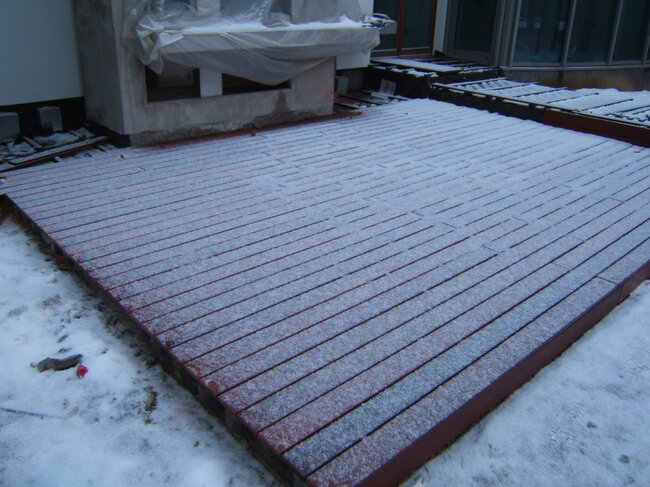 A snow-dusted wooden deck patio outside a building in winter.
