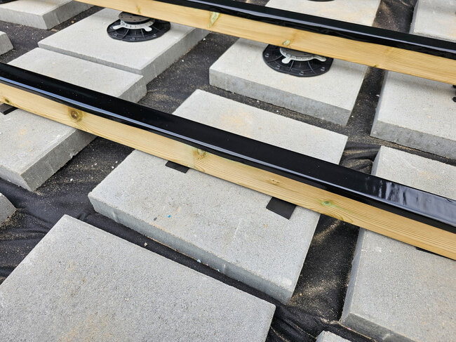 Soportes regulables y fundamentos de placas de hormigón para terraza que sostienen vigas de madera de terraza.