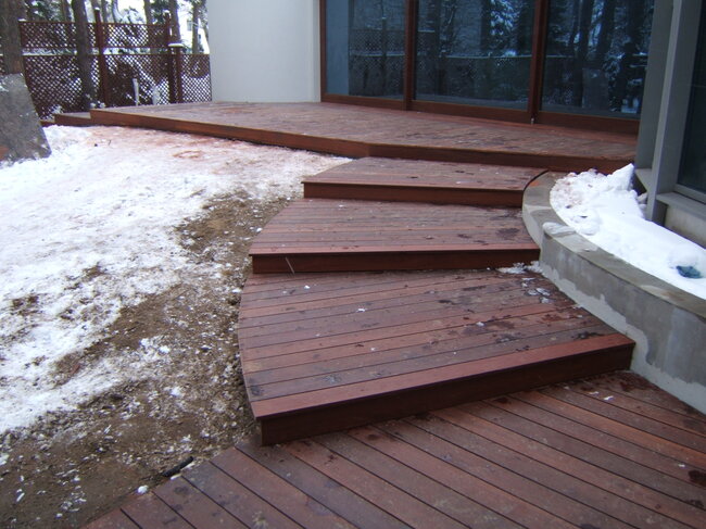 Escalones de madera curvados de terraza que conducen a una terraza exterior rodeada de nieve en invierno.