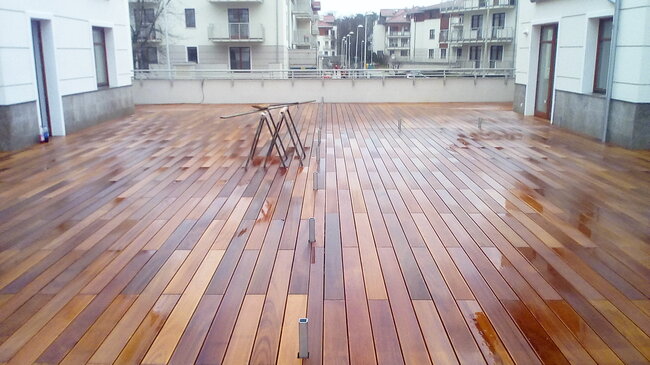 terraza de madera pulida en el patio de un complejo de apartamentos con tablas mojadas y caballetes de obra.