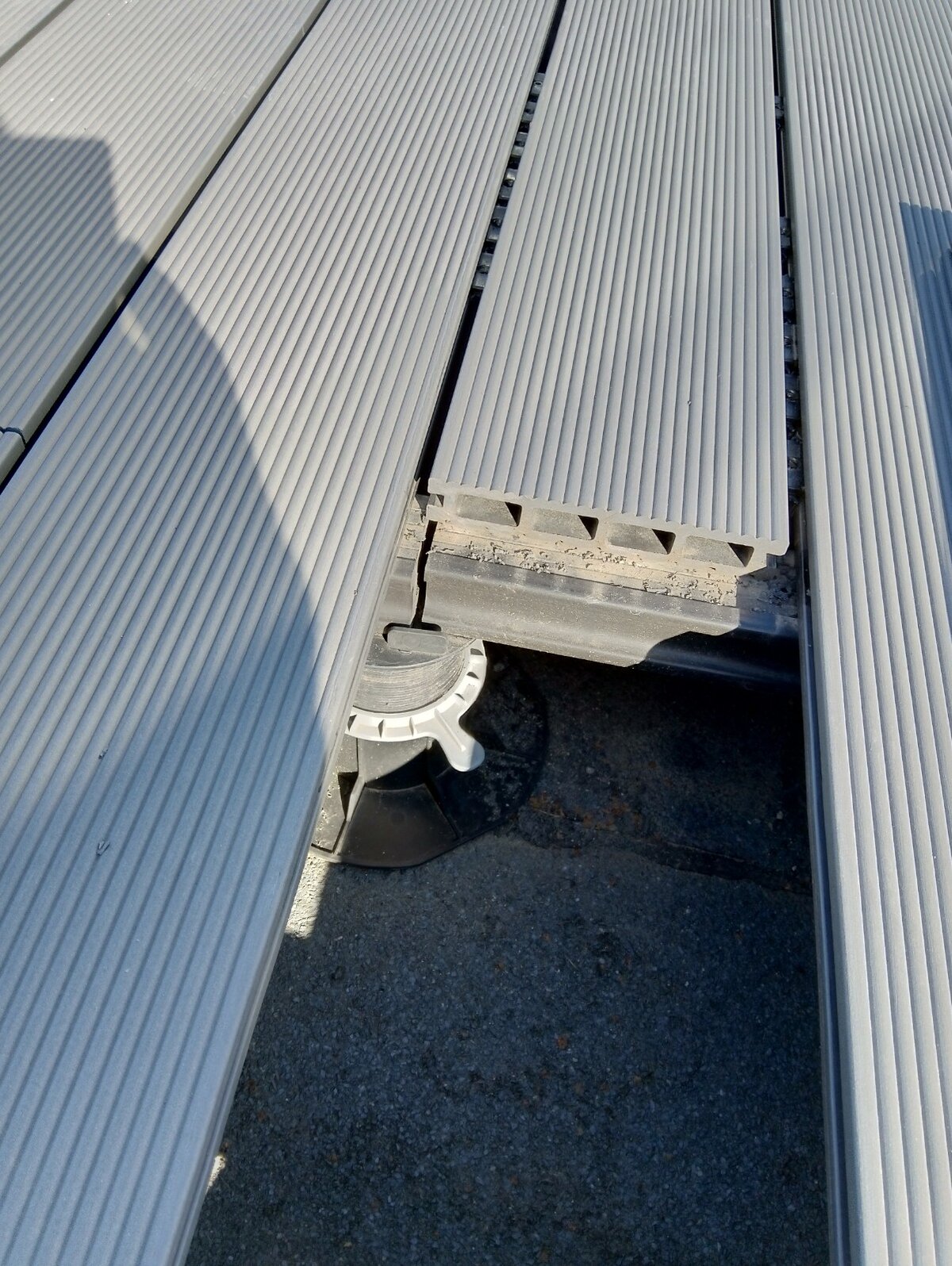 Primer plano de tablas de terraza compuestas grises ranuradas instaladas sobre un plot soporte de terraza regulable.
