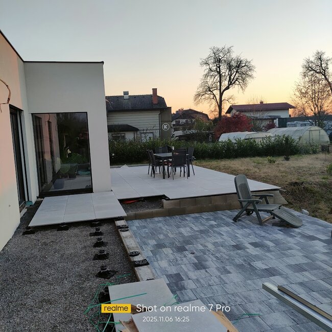 Instalación moderna de patio que muestra baldosas elevadas montadas sobre plots soporte regulables junto a una sección pavimentada con adoquines.