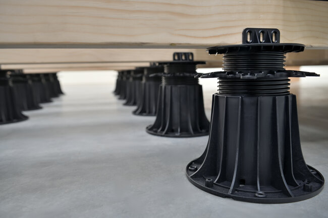 Vigas de madera para terraza apoyadas sobre plots soporte regulables de plástico negro.
