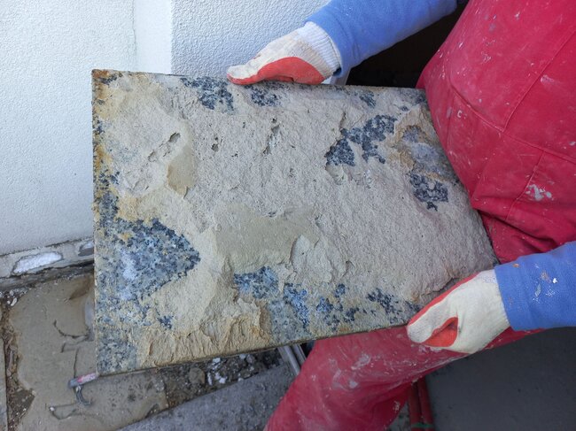 Trabajador sosteniendo una baldosa de granito dañada con restos de adhesivo en la parte inferior.