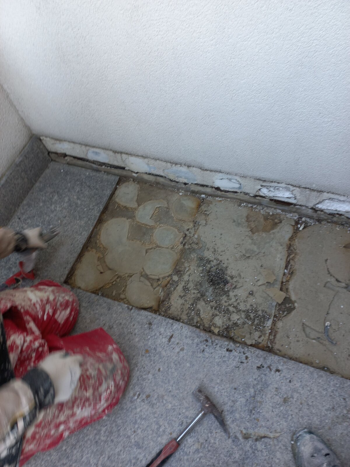 Trabajador retirando baldosas de piedra dañadas y mortero adhesivo durante la reparación de una terraza.